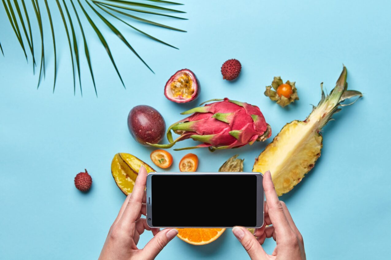 In the women hand is mobile, many different exotic fruits on a blue background decorated with